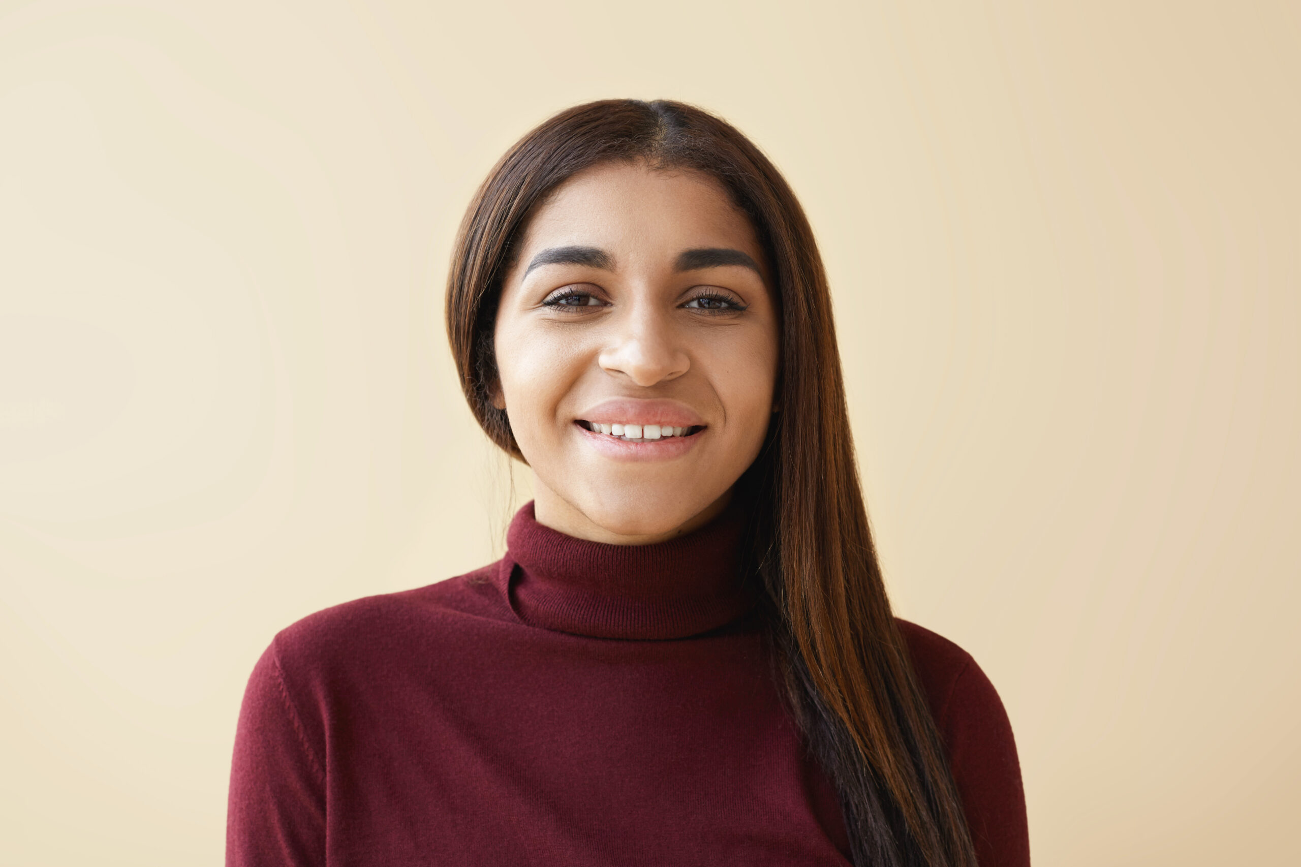 close up shot of friendly looking elegant young african american female with straight dark straight hair having happy joyful look posing at blank studio wall with copy space for your information